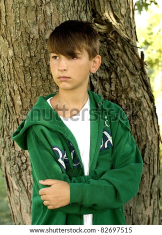 Young teen boy standing by tree in deep thought