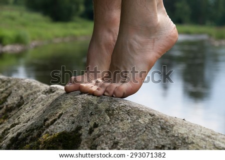 man standing on foot on stone at river doing yoga