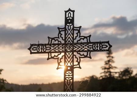 sun shining during sunset through decorated iron cross on cemetery feels sad and frustrated