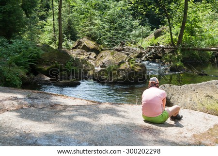 middle age women sitting on rock at stream in nature and watching calm nature forrests and meditate