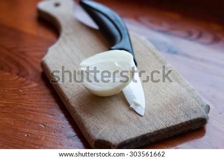 cutting  a white onion on wooden breadboard with ceramic knife
