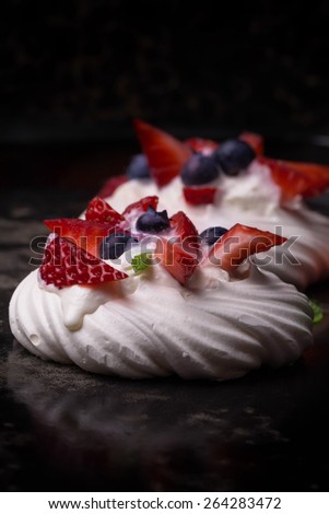 Pavlova berry cake with blueberries, strawberries and raspberries and whipped cream on the blue ceramic tray