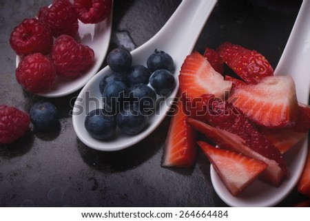 Ingredients for pavlova cake: strawberries, blueberries and raspberries in white ceramic spoons on a vintage metal tray