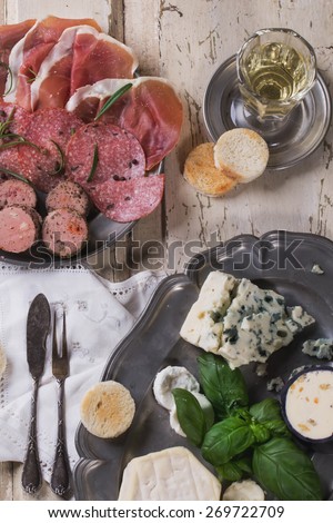 A set of various French and Italian cheeses and meats on the vintage metal plate, served with white wine, herbs and croutons
