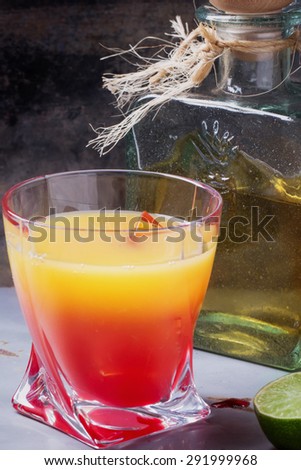 Tequila Sunrise served in a highball glass with ice, grenadine and lime
