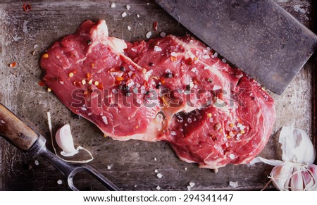 Raw fresh meat Ribeye Steak, with seasoning and meat axe and fork on vintage metal tray