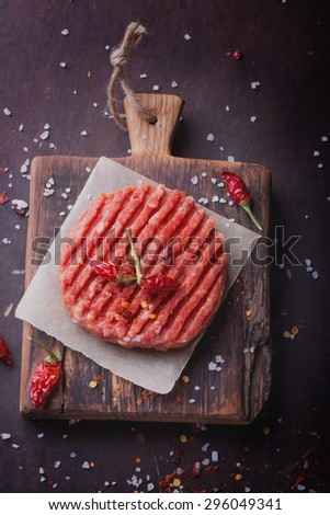 Raw Ground beef meat Burger steak cutlets with seasoning on vintage wooden boards, black background, top view