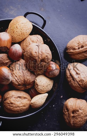 Selection of various nuts: almonds, Brazilian, walnuts in the tiny vintage spanish black metal plate, black background, top view