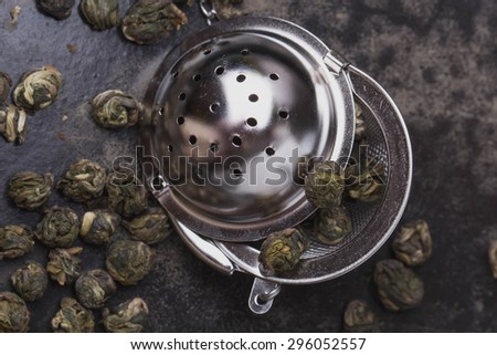 Green tea pearls in the vintage metal strainer on the black metal tray