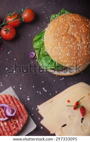 Raw Ground beef meat Burger steak cutlets with seasoning, buns, cheese, tomatoes, onion rings and salad on  black background,