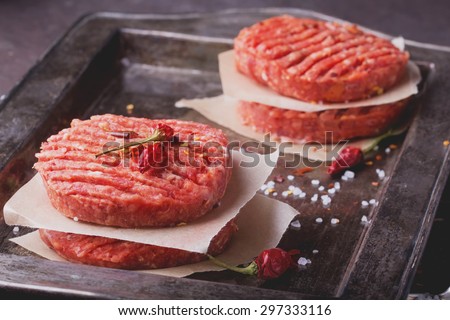 Raw Ground beef meat Burger steak cutlets with seasoning on vintage metal tray, black background