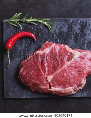 Raw Irish Sirloin Beef Steak on a slate stone board ready to be roasted with rosemary, chili pepper and salt