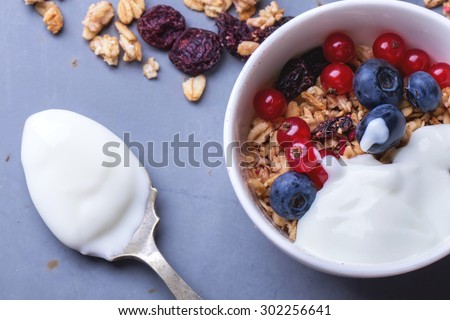 Home Made Granola breakfast with white plain yogurt, blueberries, redcurrant and dry cherries on metal background