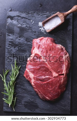 Raw Irish Sirloin Beef Steak on a slate stone board ready to be roasted with rosemary, chili pepper and salt
