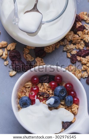 Home Made Granola breakfast with white plain yogurt, blueberries, redcurrant and dry cherries on metal background