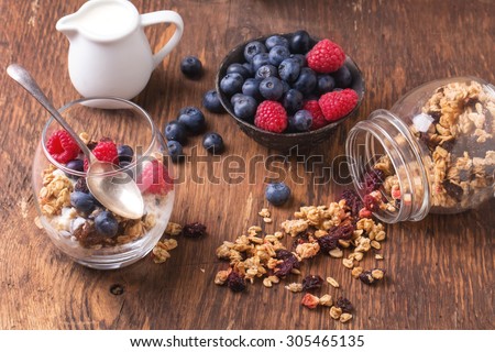 Home Made Granola breakfast with white plain yogurt, blueberries, raspberries and dry cherries on rustic wooden background