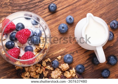 Home Made Granola breakfast with white plain yogurt, blueberries, raspberries and dry cherries on rustic wooden background, selective focus