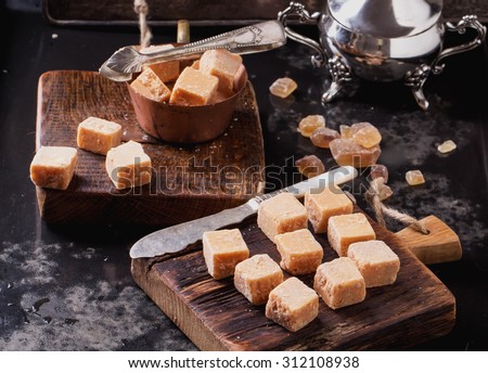 Rustic wooden boards with fudge candy silver sugar bowl, served with sugar cubes over dark background