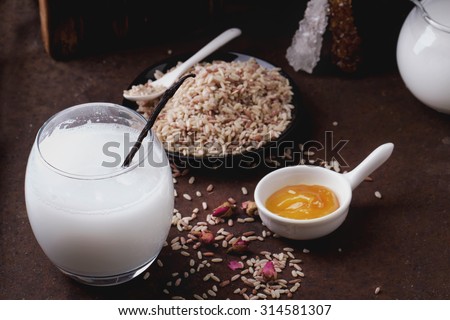 A glass of home made rice milk served with brown rice, honey and organic sugar candies on a rustic metal background