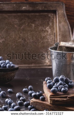 Organic blueberries served in a black vintage bowl and rustic wooden board with vintage cup and metal bucket with a scoop on a background
