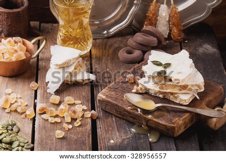 Traditional Spanish Christmas candy turron served on rustic wooden board with honey, pumpkin seeds and sugar candies. Dark rustic style