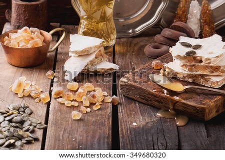 Traditional Spanish Christmas candy turron served on rustic wooden board with honey, pumpkin seeds and sugar candies. Dark rustic style