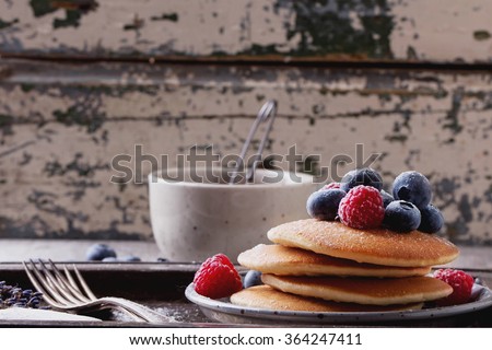 Home-made breakfast or brunch: american style pancakes served with berries and sugar powder on vintage metal tray with a cup of black tea