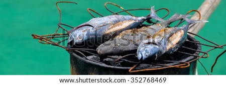 Fish barbecue on a grill top of barrel in wooden boat in front of turquoise water