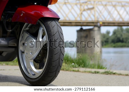 Motorcycle front wheel. Closeup of a front wheel with tyre on a motorbike. Behind the motorcycle is river. Photographed on a nice sunny day, around 11 a.m.
