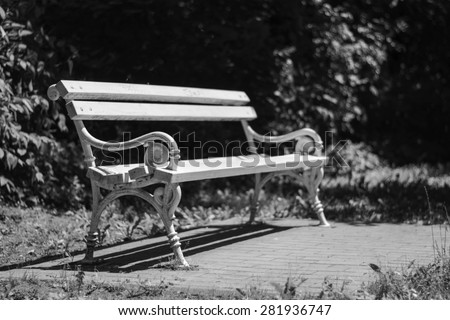 White iron park bench photographed in city park Palic, Serbia. Still in usable condition. Picture taken on nice sunny day. Black and white photo.