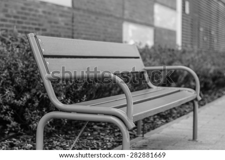 Park bench in city center. Photo was taken in Szeged, Hungary. Selective focus. The bench is madeof iron and wood. Black and white.