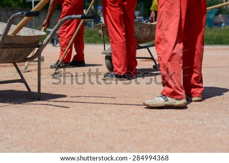 Close up of construction workers on construction site. They all wear red trousers. They standing next to iron carts.