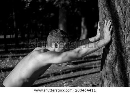 Man photographed in street workout session. Straching and straining with the help of tree. Photo was taken in early morning, around 6am in city park Dudova forest. Black and white photo.
