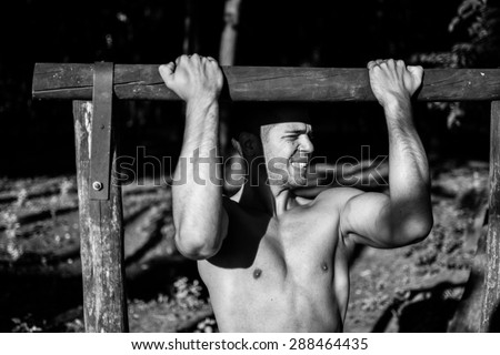 Man photographed in street workout session. Working chin-ups. Photo was taken in early morning, around 6am in city park Dudova forest. Black and white photo.