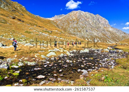 Group of hiking tourists goes along a small mountain river. Picture was taken during trekking hike in scenic Caucasus mountains at autumn, Arhiz region, bishira-Ahuba range, Karachay-Cherkessia,Russia