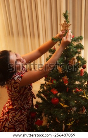 Happy woman putting star on the family Christmas tree.