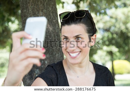 Smiling girl does selfie with his smartphone. a woman smiling at the park relaxes and takes picture. a girl at the park makes a video call with a friend and her boyfriend.