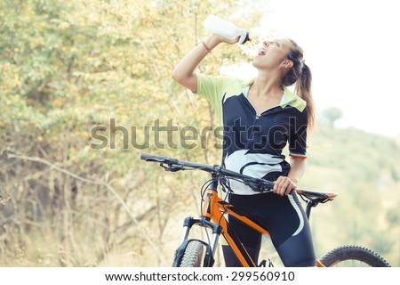 sporty girl drinking from water bottle during a tour in mountaunbike.woman practicing mountain hill in a sunny day, natural background of flowering trees. break during a bike ride in the hills.