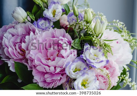 Rich bunch of pink peonies and lilac eustoma roses flowers, green leaf in glass vase. Fresh spring bouquet. Summer Background
