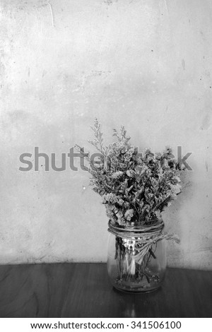 Dried flowers in glass jar on a wood table stucco wall  and black and white background