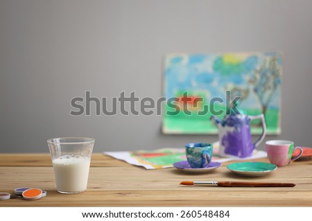 a glass of milk on wood table with paint, brush and paintings