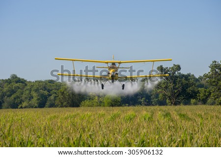 A crop duster applies chemicals to a field of vegetation.