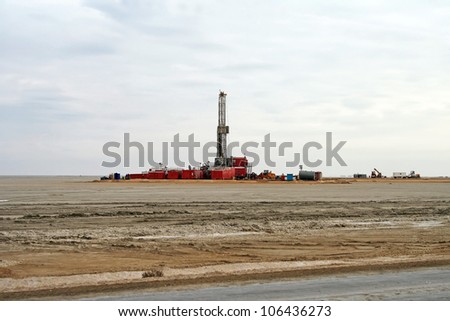 Looking across flat arid remote terrain to an operative drilling rig in the North Buzachi oil field