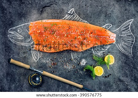 raw salmon fish steak with ingredients like lemon, pepper, sea salt and dill on black board, sketched image with chalk of salmon fish with steak and fishing rod