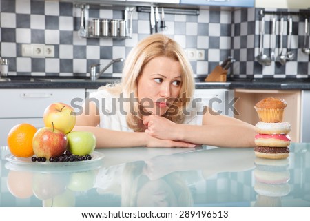 Woman choosing between fruits and cakes in the kitchen
