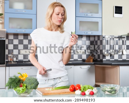 Young woman cutting vegetables in kitchen and testing piece