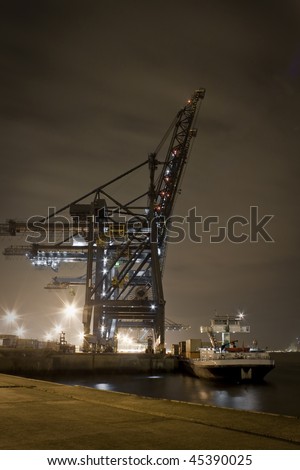 A pier at night in action, a container ship gets loaded for it\'s next task