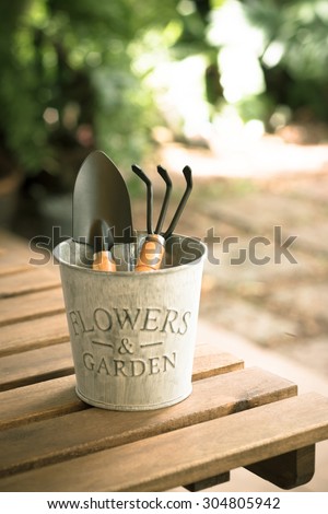 Shovel and gardening fork in bucket on wooden table in garden - vintage style effect picture