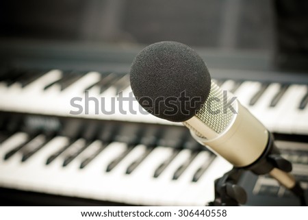 Close up on a microphone during recording session with a singer, piano in the background