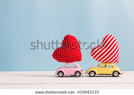 Miniature pink and yellow cars carrying heart cushions